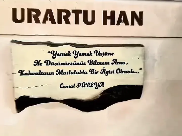 Urartu Han duvar yazısının altında, Cemal Süreya imzalı “Yemek yemek üstüne ne düşünürsünüz bilmem ama, kahvaltının mutlulukla bir ilgisi olmalı” sözünün yazılı olduğu ahşap levha.