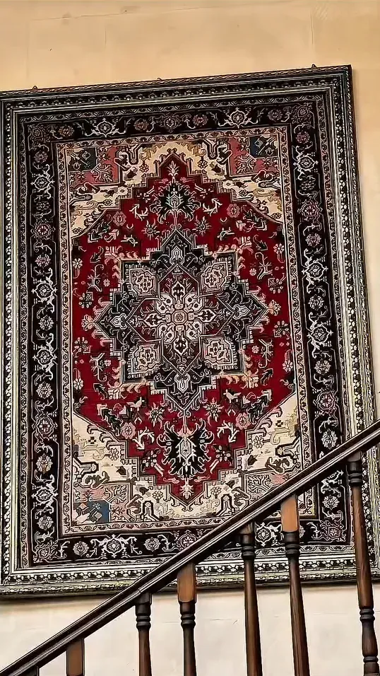 Urartu Han içinde taş duvarda çerçevelenmiş kırmızı desenli kilim ve ahşap merdiven korkuluğu.
